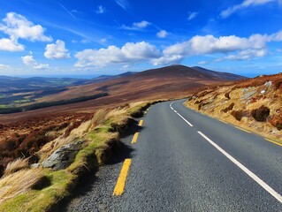 A winding road through mountainous terrain under a bright blue sky with fluffy clouds