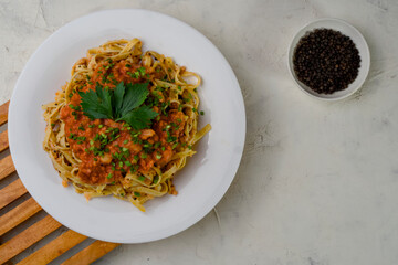 flat lay of a plate of spaghetti topped with tomato sauce mixed with meat, cheese, spices, onions and lettuce leaves stands on a wooden tray and black pepper next to it.