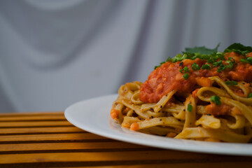 close up of a plate of spaghetti highlighting the tomato sauce mixed with meat, spices and lettuce leaves.