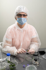 A researcher in protective gear examines aloe plants in a laboratory. The workspace features petri dishes, tools, and a microscope, highlighting the scientific study of plant applications.