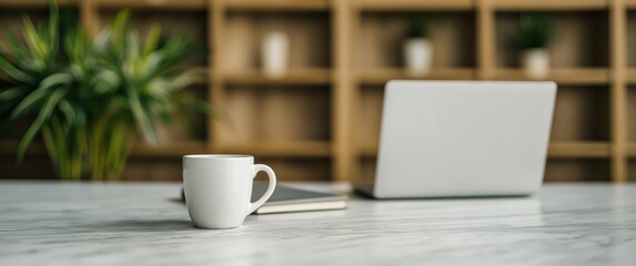 White coffee cup with laptop and tablet on marble table with wooden shelves and green plant in background for remote work and study