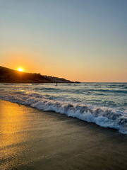 Sunset waves on a foamy beach, Greece. Summer vacations in a greek island. Golden light reflection on shallow water