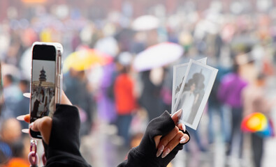 A young Chinese girl with long, well-manicured white-painted nails recreates an old Polaroid snapshot on her smartphone against a temple - China