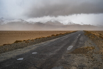 Stunning panoramic view of a distant snow-capped mountain range under a dramatic sky along the Pamir Highway, highlighting the vastness of the Tajikistan wilderness