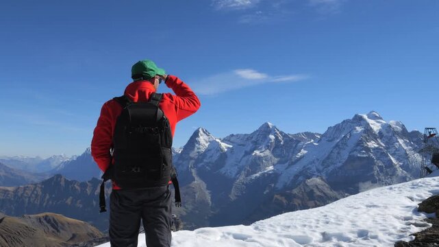 Man wearing a backpack looking at the Eiger, Monch, and Jungfrau mountains in Switzerland