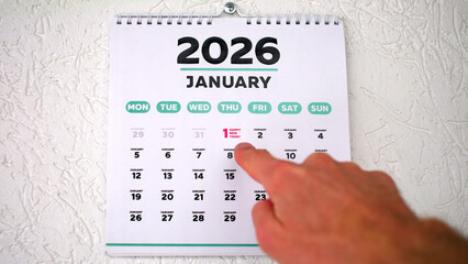 A male hand pointing finger to the date of January 1st highlighted on a wall calendar 2026