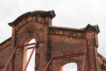 Historic brick building ruins with exposed archways and structural supports, showcasing weathered textures and architectural details in a cloudy sky backdrop, evoking a sense of nostalgia