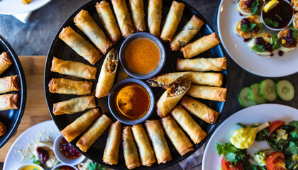 Assorted spring rolls and dipping sauces beautifully arranged on a table with fresh salads