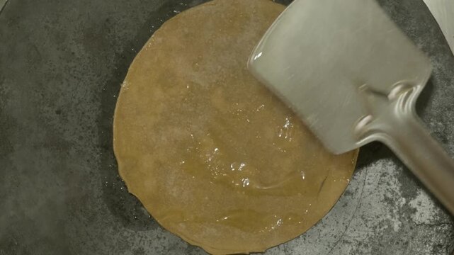 Cooking Roti on Hot Tawa with oil and steel spatula or palta. internal shot, top view shot, 4k.