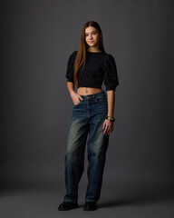 Young woman in a black puff-sleeve crop top and wide-leg jeans against a gray background. Stylish teen fashion look.