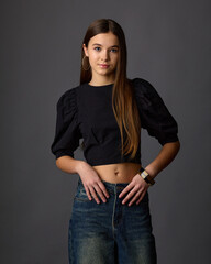 Young woman in a black puff-sleeve crop top and wide-leg jeans against a gray background. Teen fashion style.