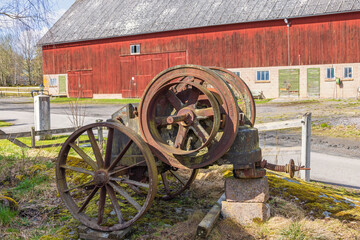 Fototapeta premium Old rusty rock crusher by a red barn in the countryside