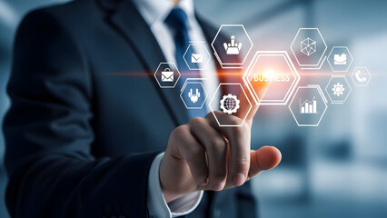 Businessman pointing to a holographic interface displaying business icons and the word business on a glowing hexagon