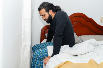 Person sitting on bed with bowed head and white comforter.