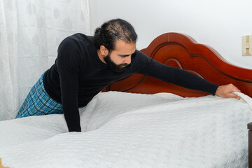 Person pulling white quilted bedspread over mattress in bedroom.