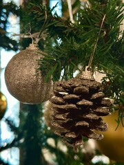 Evergreen branches of a Christmas tree are decorated with a glittery spherical ornament and a frosted pine cone.