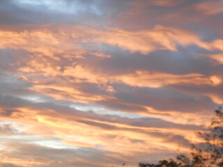 Obraz premium A dramatic sunset or sunrise sky featuring vibrant orange, yellow, and deep gray clouds over the silhouette of a mountain peak. The warm light creates a striking, intense atmosphere