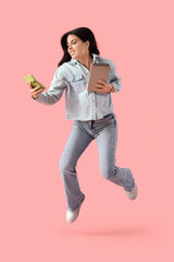 Naklejka premium Beautiful young woman with notebook and calculator jumping on pink background