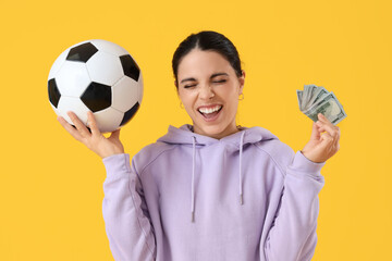 Happy young woman with money and soccer ball on yellow background. Sports bet concept