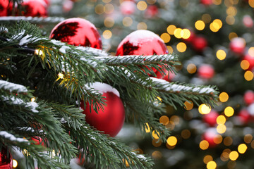 Christmas tree with red toy balls and festive illumination, golden lights on background. New Year decorations on city street covered with snow