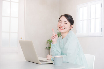 自宅やカフェでパソコンをする笑顔のかわいい女性　　　指差しでポイントのポーズ