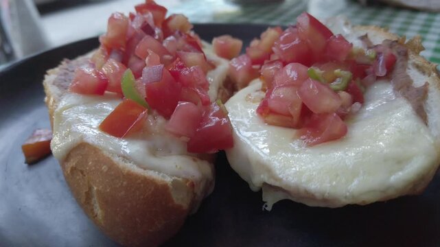 Pull-back close-up showing melted cheese mollete toasts topped with fresh tomato mix