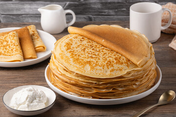 Stack of golden crepes served with sour cream on a wooden table