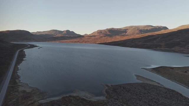A road along mountain lake and surrounding mountains at sunset in Norway. Drone footage
