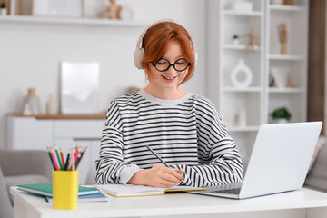 Teenage redhead girl with notebook and laptop studying at home