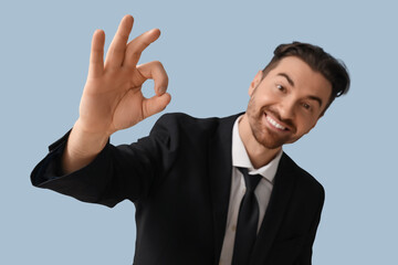 Handsome young businessman showing OK gesture on grey background