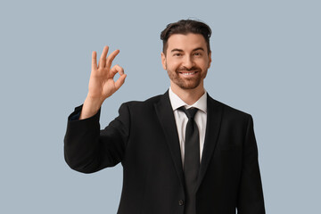 Handsome young businessman showing OK gesture on grey background