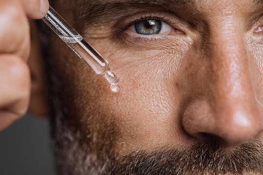 Close up of man applying facial serum with pipette for skincare and anti-aging routine