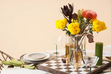 Fotobehang Eetkamer Stylish dining table setting with colorful flower bouquet, chessboard centerpiece, glassware and candle in warm modern interior with copy space  © Pixel-Shot
