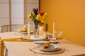 Beautiful table setting with bouquet of flowers and candles near orange wall, closeup