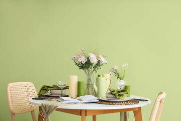 Beautiful table setting with bouquet of flowers and candles near green wall