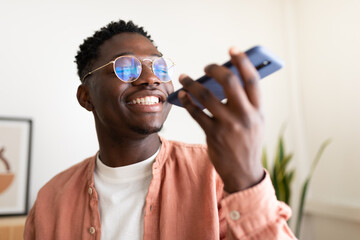 Smiling young man recording voice message on smartphone at home