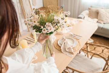 Young woman serving table with beautiful flowers in dining room, closeup