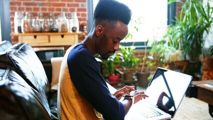 Man is checking smartwatch while working on laptop on sofa in flat design loft, technology theme