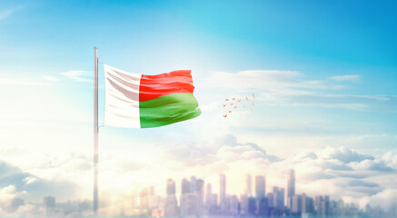 Madagascar  flag wavering in beautiful clouds with building skyline. The flag with drone shot in beautiful sky. Madagascar national flag for independence day.