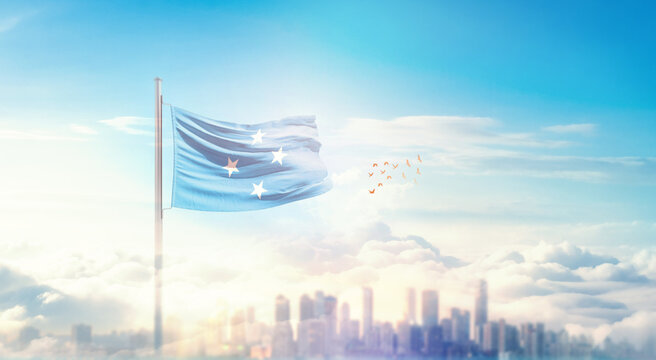 Micronesia flag wavering in beautiful clouds with building skyline. The flag with drone shot in beautiful sky. Micronesia national flag for independence day.