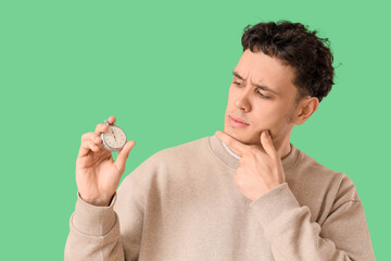 Thoughtful young man with stopwatch on green background