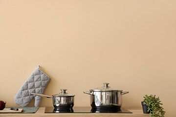 Stainless cooking pots on electric stove near beige wall