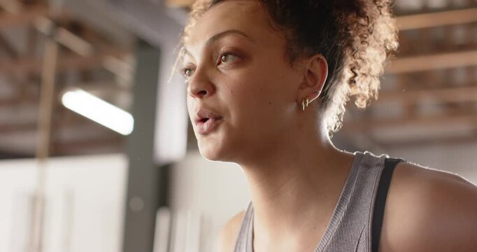 After set African American woman pausing by large windows listening trainer before resuming workout