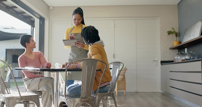 Female server responding to couple request and scrolling tablet menu at home dining table