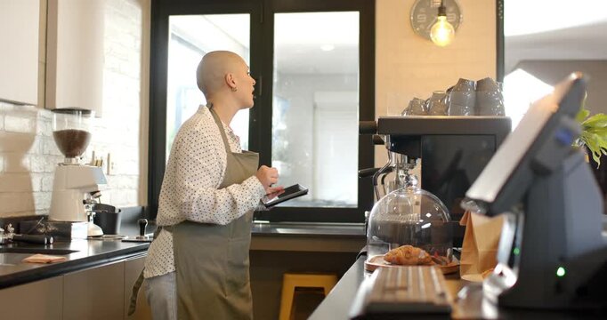 Tablet pinging woman tapping screen at cafe counter pointing to espresso machine confirming order