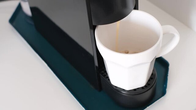 Coffee from capsule coffee machine is poured into white cup.
