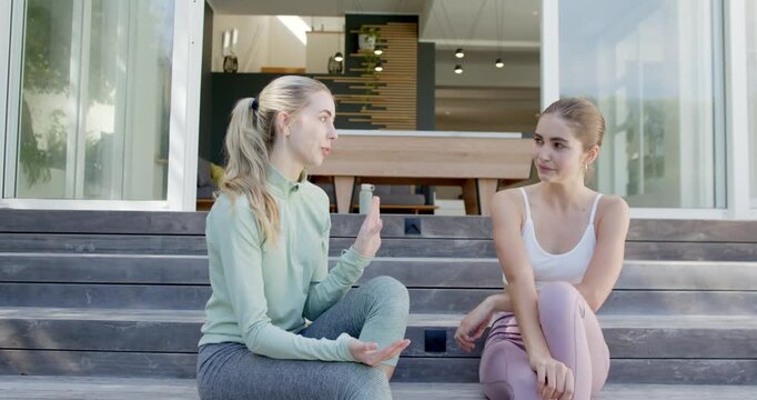 Female friends starting conversation on wooden patio steps using gestures high fiving and laughing