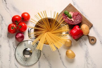 Cooking pot with different vegetables, pasta and beef on marble background