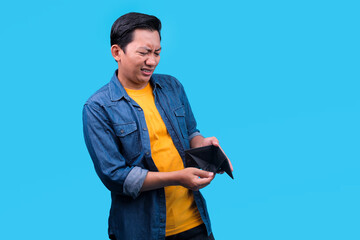 Sad Young Asian Man With an Empty Wallet, Showing Stress on Blue background