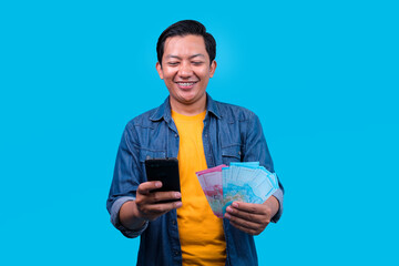 Young Man Using Mobile Cell Phone While Holding Fan of Cash Money in Rupiah